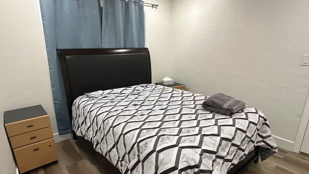 Ein Schlafzimmer mit einem Bett, einem Nachttisch, einer Kommode und einem Vorhang.