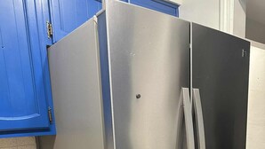 Ein Edelstahl-Kühlschrank mit Gefrierfach, blaue Schränke und eine Arbeitsplatte mit einer Schüssel und einem roten Gegenstand.