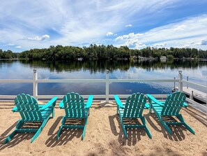 Une terrasse au bord du lac, avec trois chaises Adirondack vertes, donnant sur un lac paisible et entourée d’une balustrade blanche.