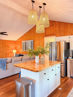 A modern kitchen with wooden walls, a central island, stainless steel appliances, and a hanging light fixture.
