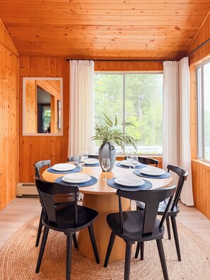 Une pièce aux murs lambrissés, avec une table ronde dressée pour quatre personnes, un vase avec une plante et un miroir accroché au mur.