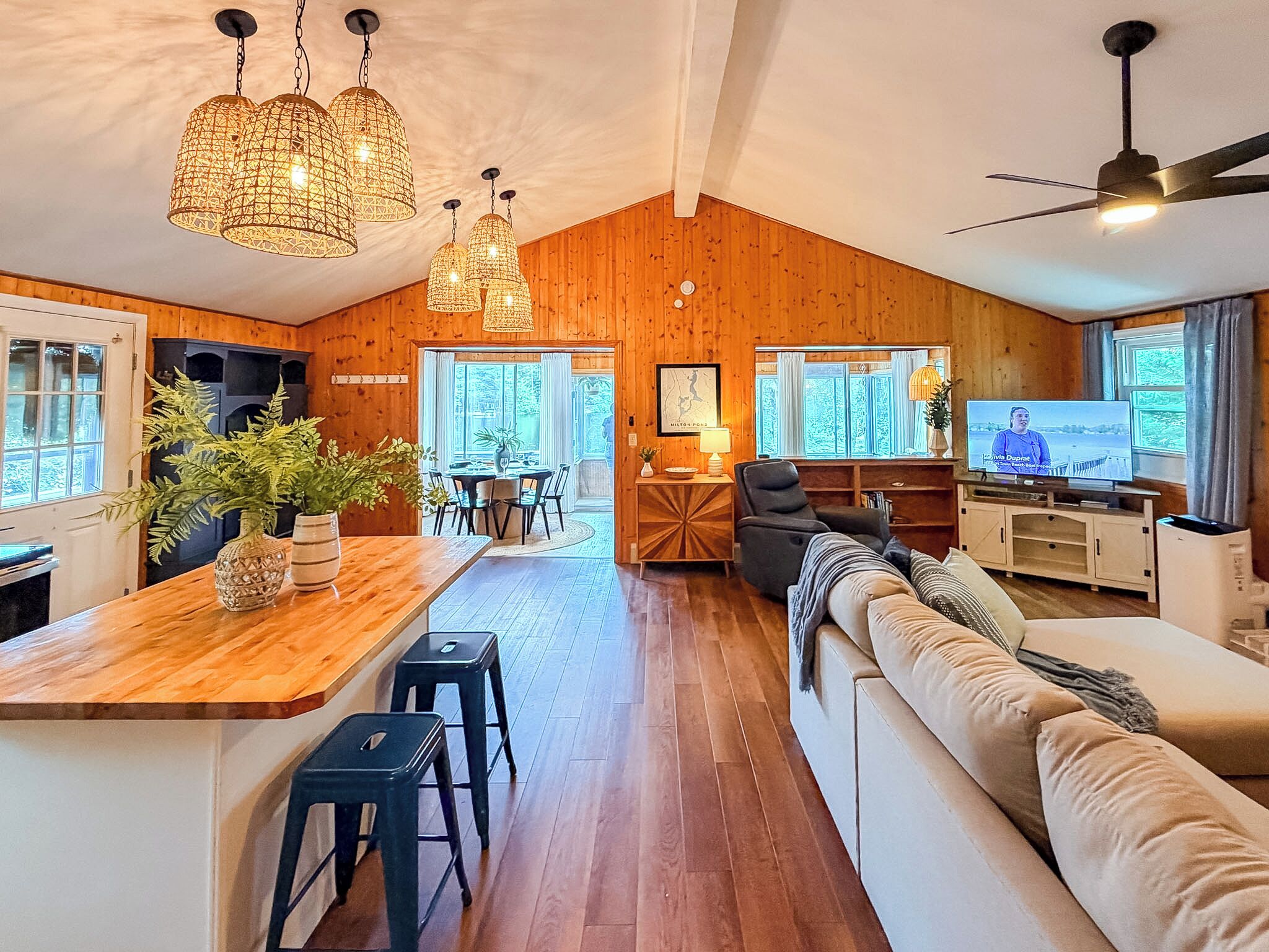 Amplia sala de estar con techo de madera, un sofá, un televisor y un comedor con mesa y sillas.