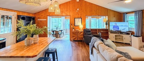Amplia sala de estar con techo de madera, un sofá, un televisor y un comedor con mesa y sillas.