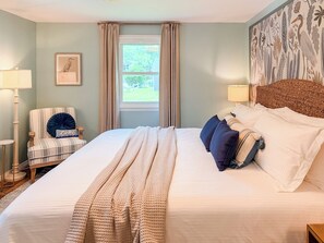 A bedroom with a bed, a chair, a window, and a wall with a nature-themed mural.