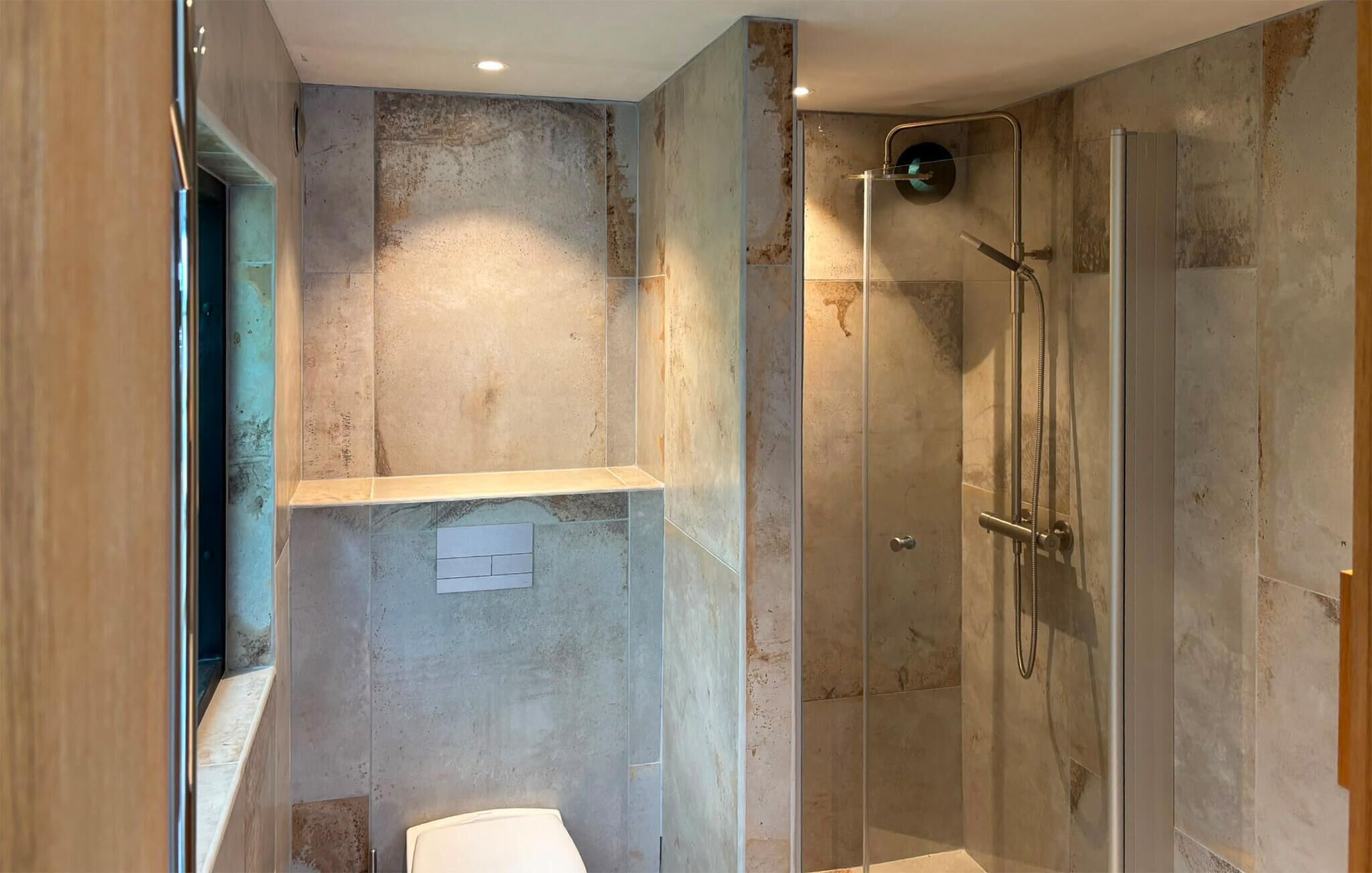 Un baño moderno con ducha de mampara de vidrio, inodoro y estante.