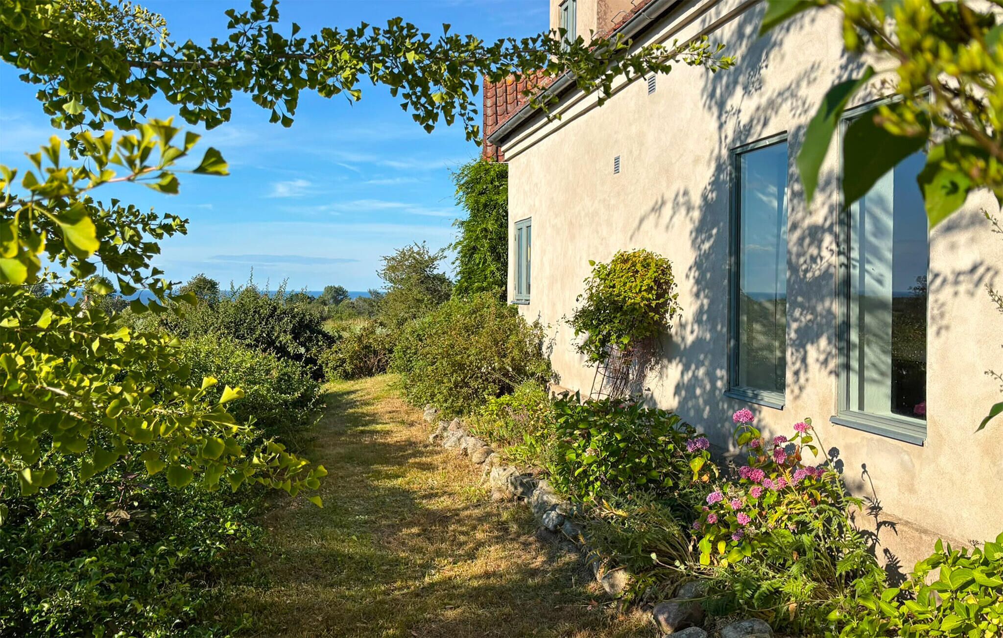 A building with a garden path leading to a window, surrounded by greenery and a clear sky.