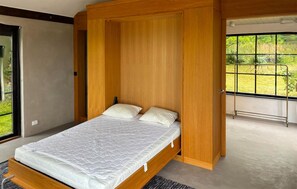 A modern bedroom with a wooden bed frame, a large window with a view of greenery, and a balcony with a metal railing. - 5 bedroom luxurious home in Simrishamn (Simrishamn)
