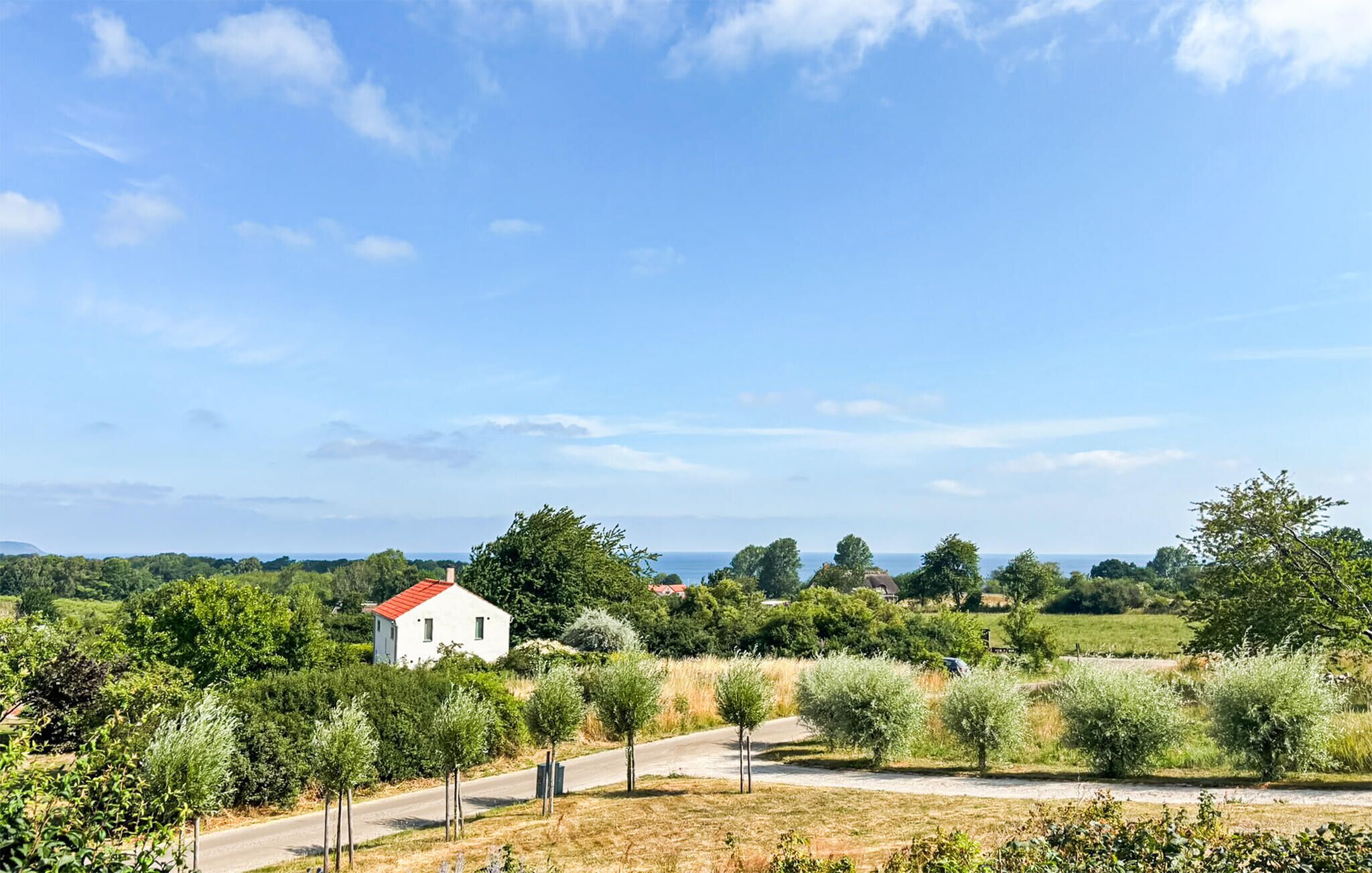 Ländliche Landschaft mit einem weißen Haus, Bäumen und blauem Himmel.