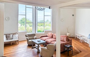 Ein großzügiger Wohnbereich mit einer Couch, Sesseln, einem Couchtisch und Blick durch große Fenster.