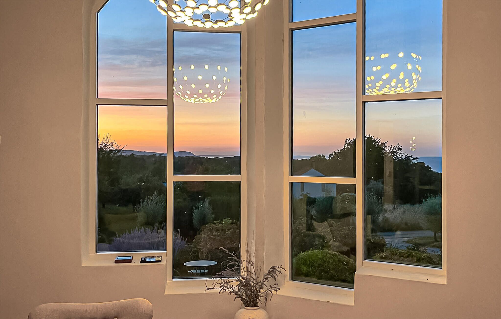 Een kamer met een groot raam dat uitkijkt op het landschap, een vaas met planten en een tafel met een stoel.