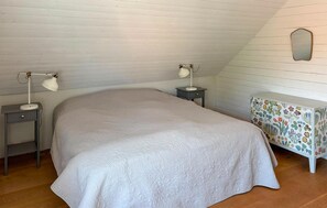 Ein Schlafzimmer mit einem großen Bett, zwei Nachttischlampen, einem kleinen Tisch mit einer blumigen Tischdecke und einem Spiegel an der Wand.