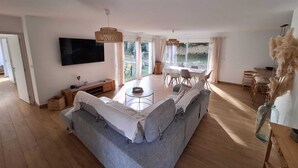 Ein geräumiger Wohnbereich mit einer großen Couch, einem Esstisch und einem an der Wand befestigten Fernseher.