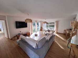 Ein geräumiger Wohnbereich mit einer großen Couch, einem Esstisch und einem an der Wand befestigten Fernseher.