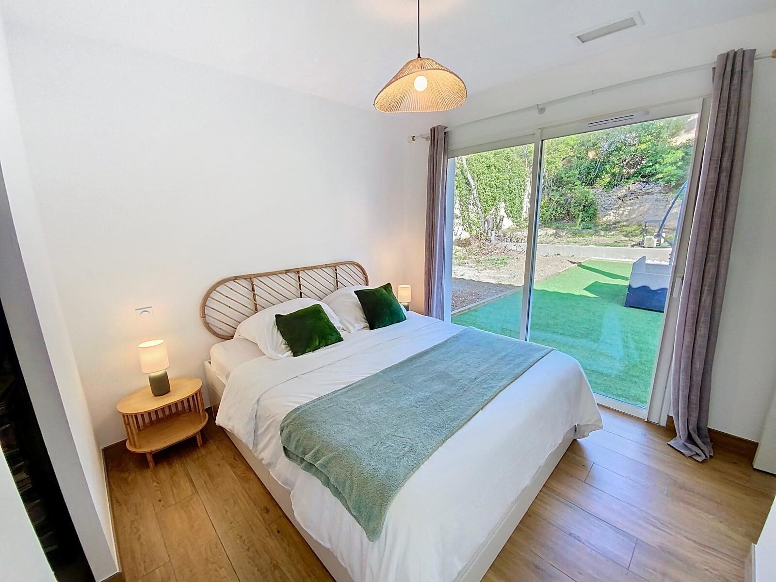 Une chambre à coucher avec un lit, des lampes de chevet et une vue sur un jardin, accessible par une porte-fenêtre coulissante.