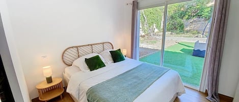 Une chambre à coucher avec un lit, des lampes de chevet et une vue sur un jardin, accessible par une porte-fenêtre coulissante.