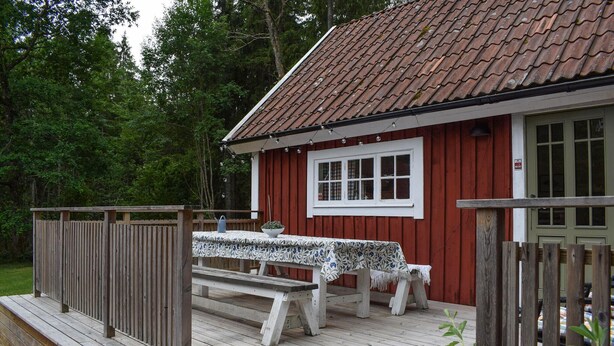 A wooden cabin with a red exterior, a white window, and a wooden deck with benches. - Lovely home in Tving with house a panoramic view (Tving)