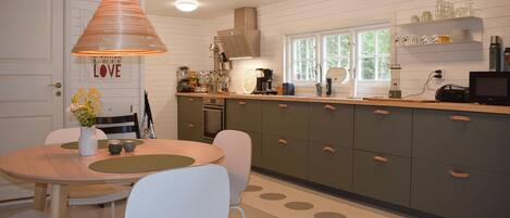 A kitchen with a wooden table, chairs, a hanging light fixture, and a window with a view.