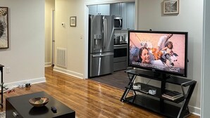 Ein modernes Wohnzimmer mit Flachbildfernseher, einem schwarzen Couchtisch und einer Küche im Hintergrund.