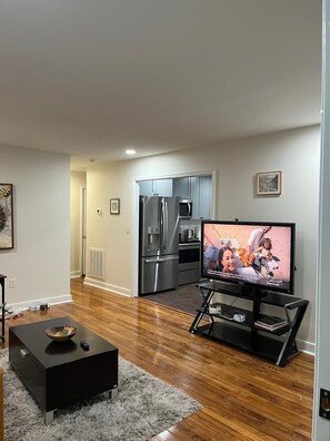Ein modernes Wohnzimmer mit Flachbildfernseher, einem schwarzen Couchtisch und einer Küche im Hintergrund.
