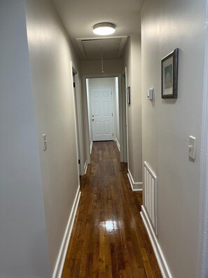 A hallway with wooden flooring, white walls, a white door at the end, and a ceiling light fixture. - Charming little house (Richmond)