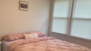 Ein Schlafzimmer mit einem Bett, einem Nachttisch, einem Fenster mit Jalousien und einem Bild an der Wand.