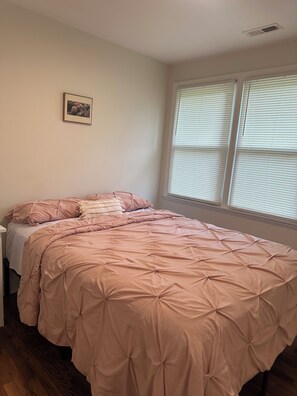 Ein Schlafzimmer mit einem Bett, einem Nachttisch, einem Fenster mit Jalousien und einem Bild an der Wand.