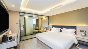 Una habitación de hotel con una cama grande, mesitas de noche, televisión y un escritorio con lámpara.