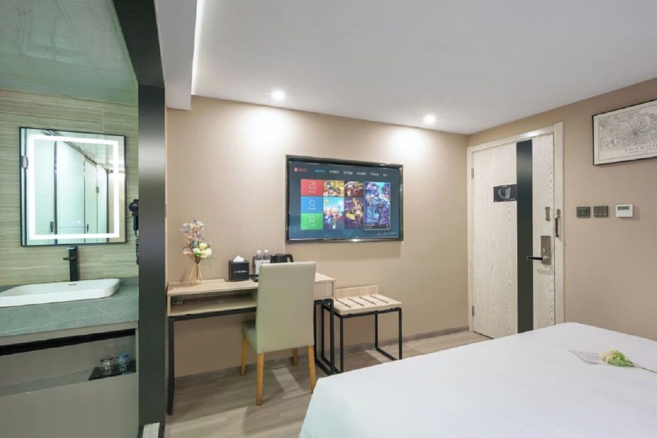 Una habitación de hotel con cama, escritorio con silla, televisor montado en la pared, baño con espejo y puerta.