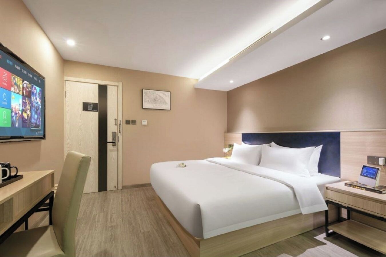 A hotel room with a bed, bedside table, TV, desk, chair, and a door.