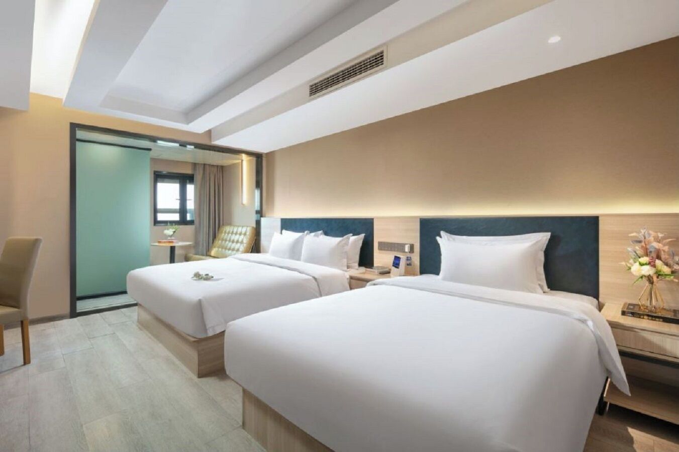 A hotel room with two beds, a desk, a chair, and a bathroom door.