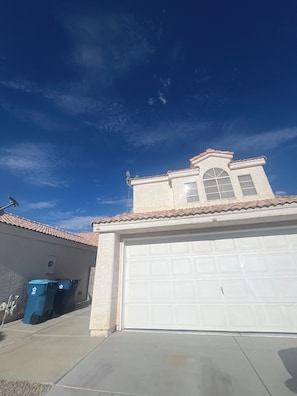 A residential garage with a white door, a satellite dish, and blue recycling bins.