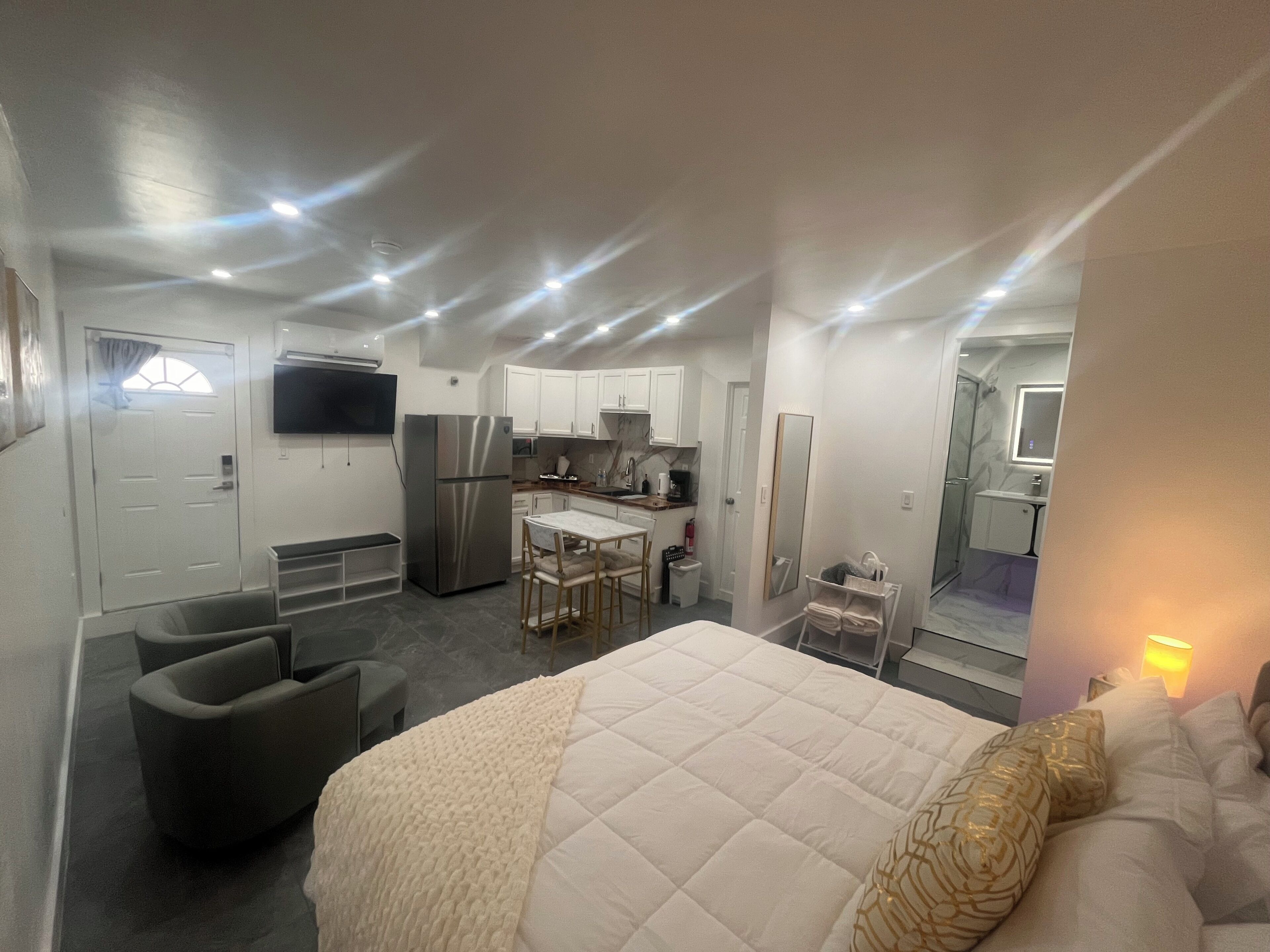 A compact hotel room with a bed, a seating area, a kitchenette, and a bathroom.