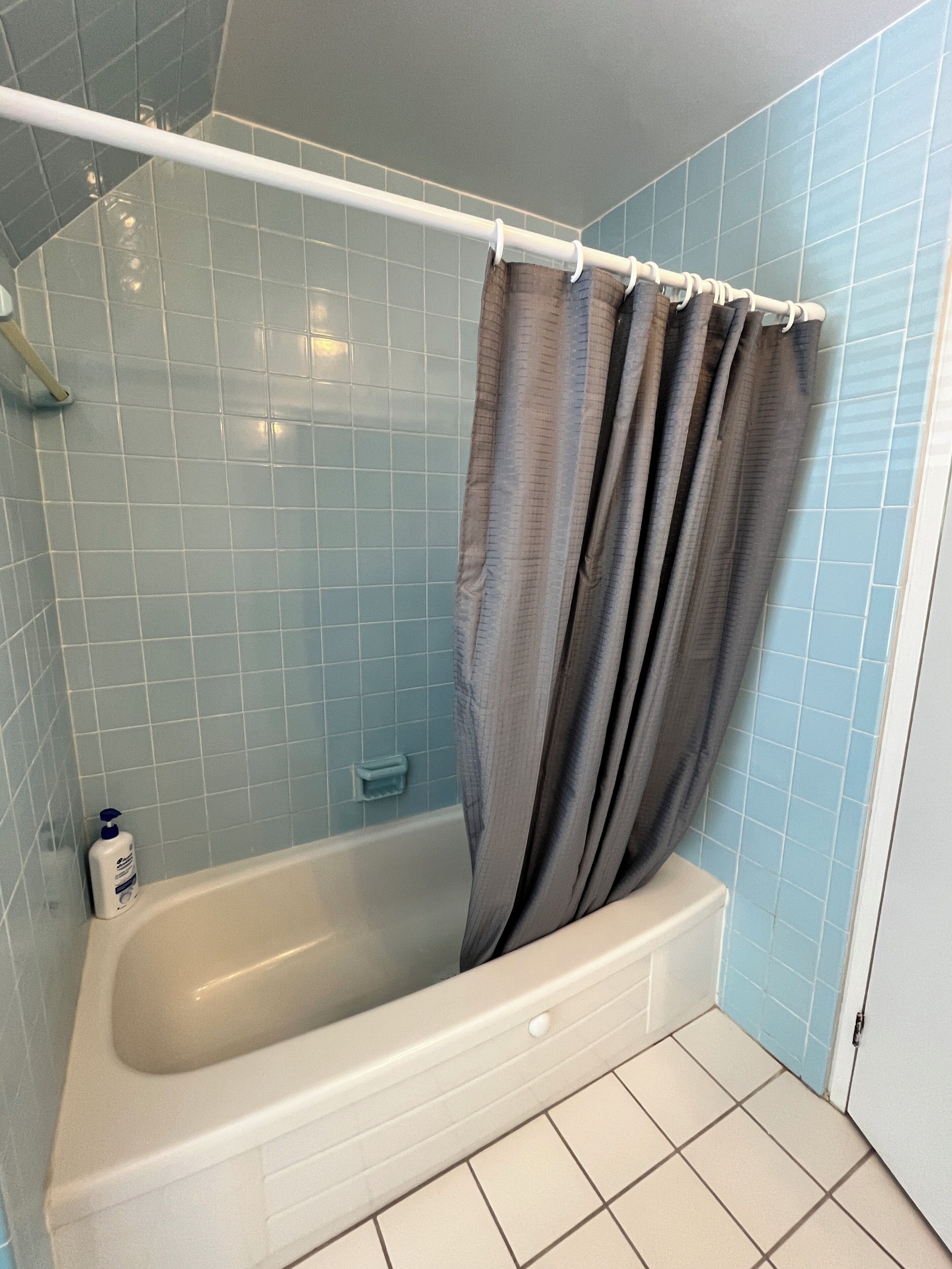 Une baignoire avec un rideau de douche, une douchette et un distributeur de savon.