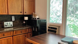 A kitchen with wooden cabinets, a countertop with a toaster, a refrigerator, and a window with a view of trees.