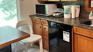 A kitchen with wooden cabinets, a microwave, a toaster, a dishwasher, and a window with a view of trees.