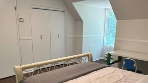 A bedroom with a bed, a chair, a desk, and a window.