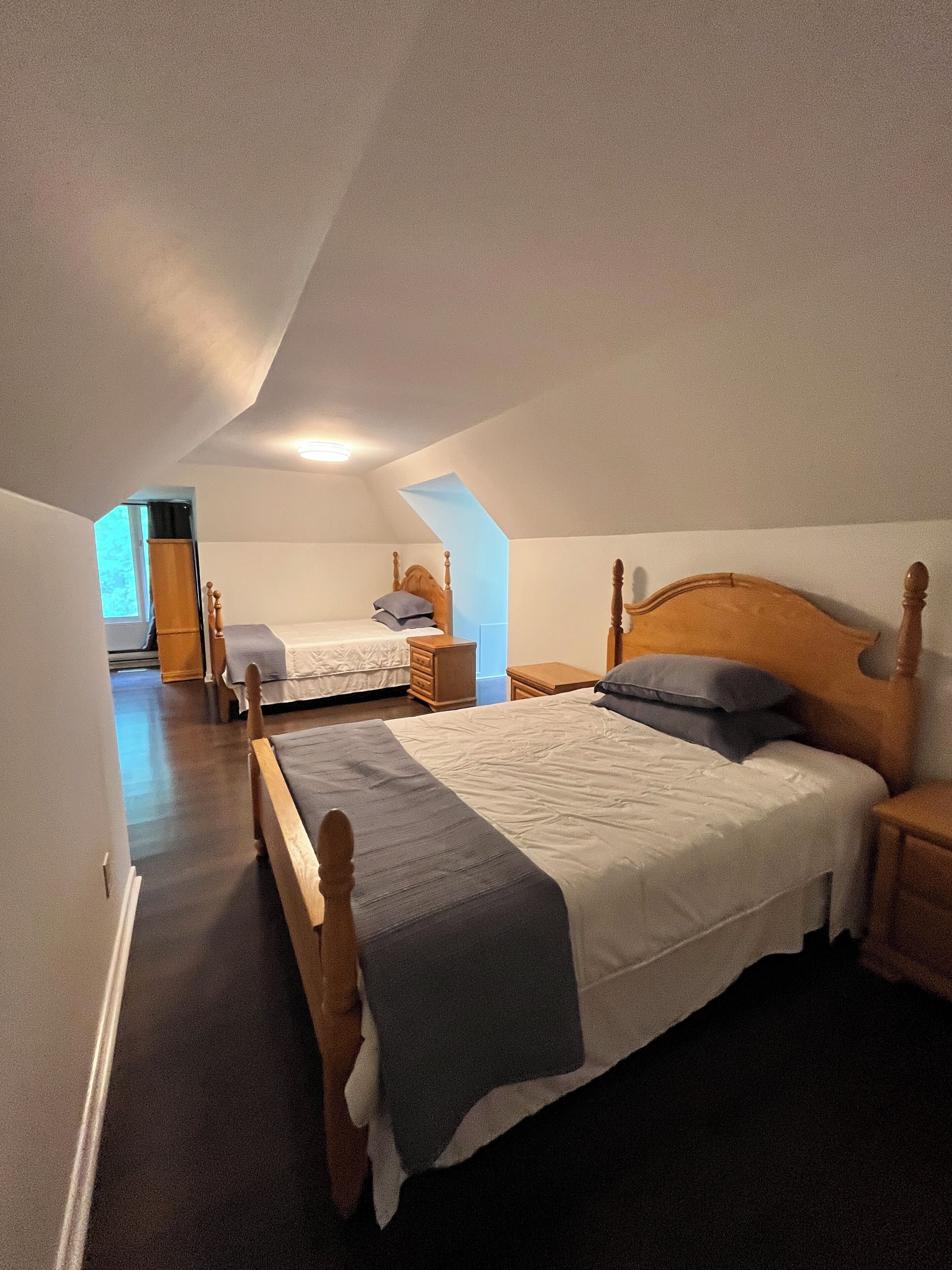 Ein Schlafzimmer mit zwei Betten, Holzkopfteilen und einer schrägen Decke.