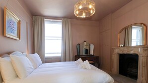 A bedroom with a large bed, a fireplace, a mirror, and a painting on the wall. - 123 On The Sea Victorias Place (Weymouth)
