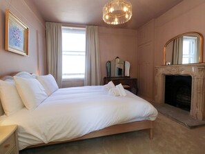 Ein Schlafzimmer mit einem großen Bett, einem Kamin, einem Spiegel und einem Gemälde an der Wand.