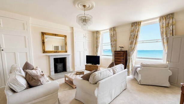 A living room with a fireplace, a television, and a view of the sea. - 123 On The Sea Victorias Place (Weymouth)
