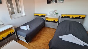 Et soveværelse med to senge, et natbord, en kommode og et vindue med persienner.