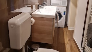 Et lille badeværelse med toilet, vask og to stablede vaskemaskiner.