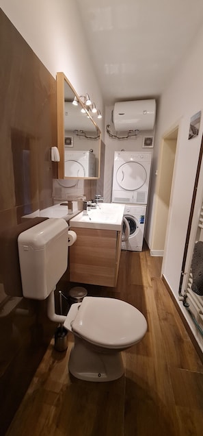 Ein kleines Badezimmer mit Toilette, Waschbecken und zwei übereinander angeordneten Waschmaschinen.
