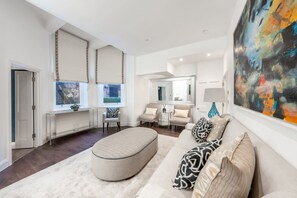 A modern living room with a sofa, ottoman, and a large abstract painting. - Luxury 2 Bedroom Apartment in the Heart of Knightsbridge (London)