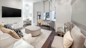 A modern living room with a flat-screen TV, a sofa set, a round ottoman, and a glass coffee table. - Luxury 2 Bedroom Apartment in the Heart of Knightsbridge (London)