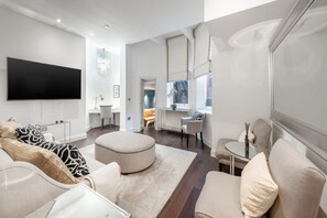 A modern living room with a flat-screen TV, a sofa set, a round ottoman, and a glass coffee table. - Luxury 2 Bedroom Apartment in the Heart of Knightsbridge (London)