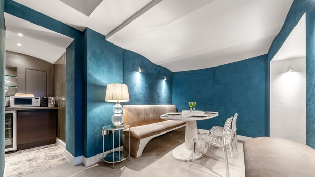A modern living room with a blue accent wall, a sofa, a round table with a lamp, and a glass coffee table. - Luxury 2 Bedroom Apartment in the Heart of Knightsbridge (London)