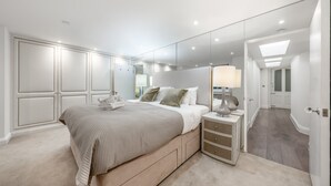 A bedroom with a large bed, bedside tables, a mirror, and a walk-in closet. - Luxury 2 Bedroom Apartment in the Heart of Knightsbridge (London)