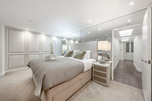 A bedroom with a large bed, bedside tables, a mirror, and a walk-in closet. - Luxury 2 Bedroom Apartment in the Heart of Knightsbridge (London)