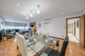 A modern living room with a glass dining table, white chairs, and a sofa. - Super Deluxe Two-bedroom Apartment (London)